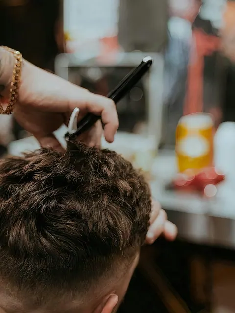 A barber shapes a client's textured haircut with scissors and comb.