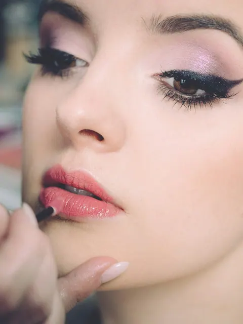 A makeup artist applies lip color to a model with a precise winged liner.
