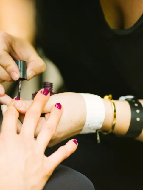 Close-up of a nail technician painting a precise, glossy manicure.