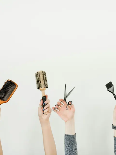 Raised hands hold brushes, scissors and combs in celebration.